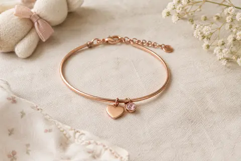 Bracelet en cuivre avec pendentif cœur et pierre de naissance, posé sur un tissu de lin ivoire.